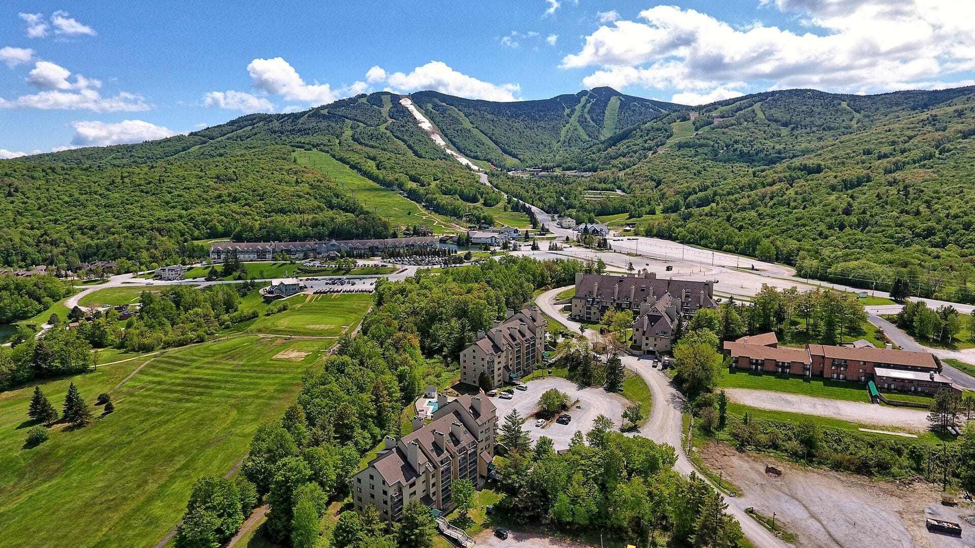 Aerial panoramic view of Mountain Green Resort condominium buildings with Killington ski resort slopes and chairlifts visible on mountain behind property